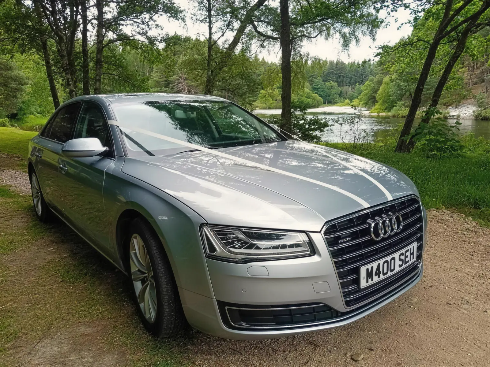 Audi A8 L with ribbons beside a wooded river